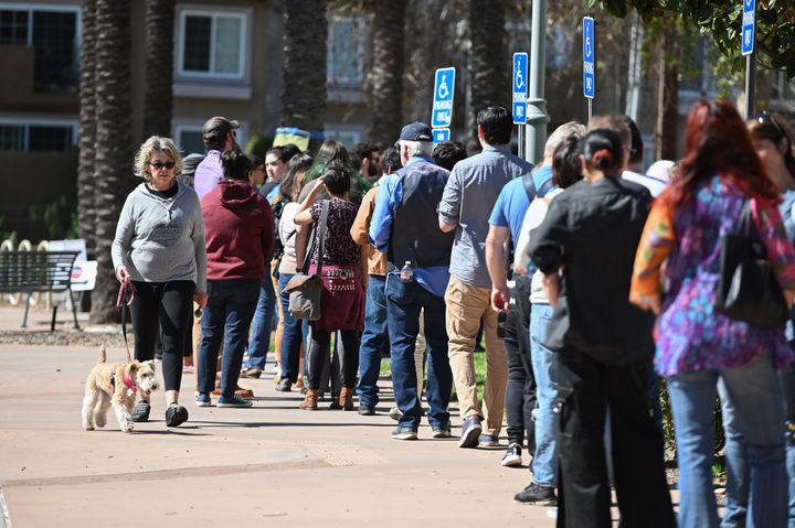 A woman walks her dog past a long line of voters waiting to cast their ballot in the presidential primary at the Buena Vista Branch Library in Burbank, California on Super Tuesday, March 3, 2020. 