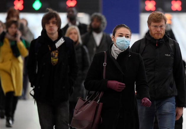 Workers, including one wearing a protective face mask, arrive during the morning rush hour at Waterloo Station in London on Wednesday 