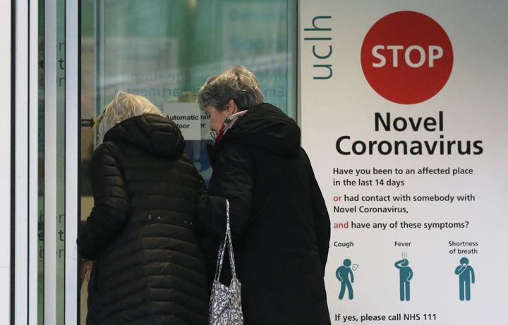 Two women walk past a sign providing guidance information about novel coronavirus in London.