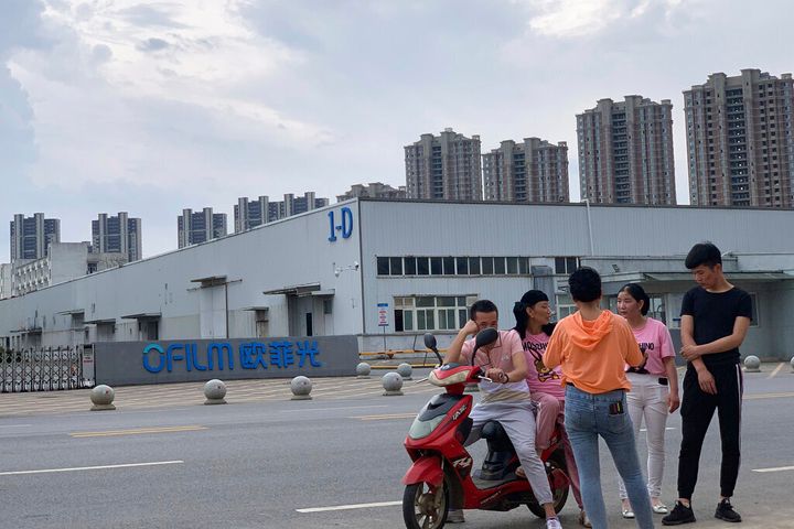In this photo taken Wednesday, June 5, 2019, neighborhood residents chat near the entrance to an OFLIM factory in Nanchang in