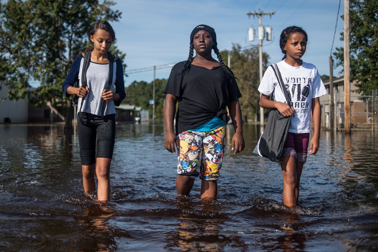 (L-R) Cassandra Rush, Anyah Carpenter, and Rosa Rush walk through floodwaters caused by Hurricane Matthew in their neighborhood on Oct. 15, 2016 in Lumberton, North Carolina.
