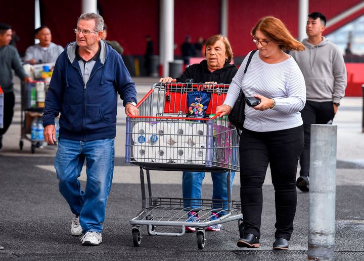 People leave a Costco warehouse with rolls of toilet paper amongst their groceries in Melbourne on March 5, 2020.