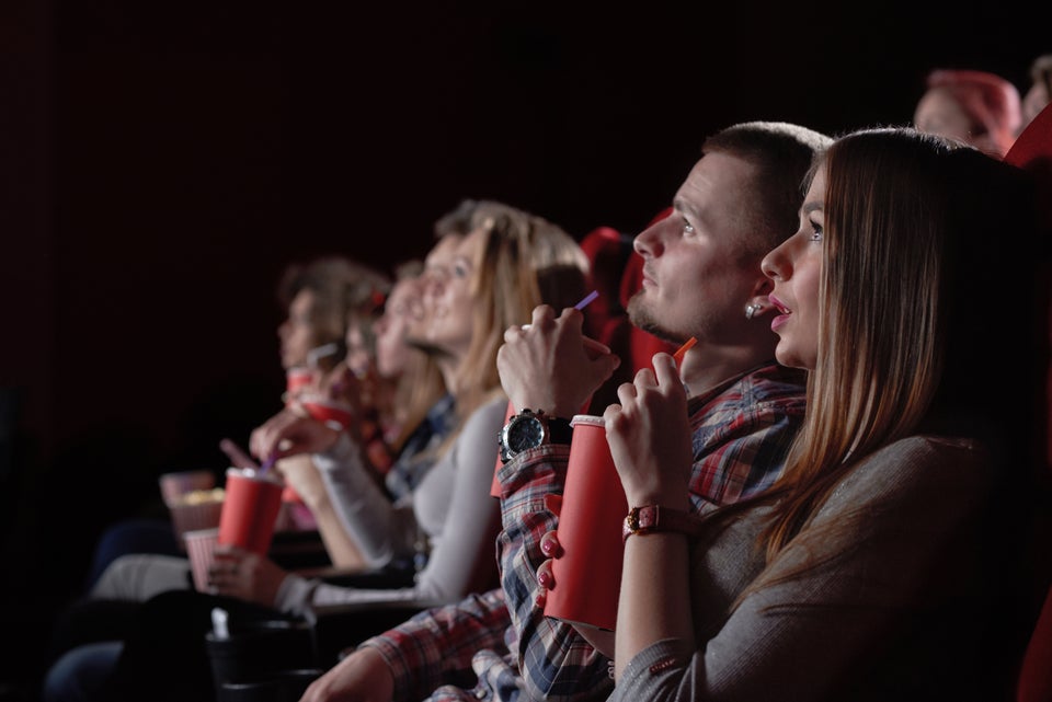 View from side of excited girl watching intriguing movie in cinema. Pretty blonde n gray shirt eating popcorn and expecting final of shocking film. Concept of fun and recreation.
