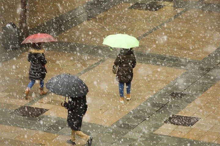 Varios transeúntes se protegen de la nieve en Vitoria.