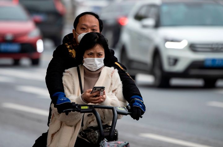 People wearing face masks ride a bike along a street in Jiujiang's central Jiangxi province on March 7, 2020. - China on March 7 reported 28 new deaths from the COVID-19 coronavirus outbreak, bringing the nationwide toll to 3,070. (Photo by NOEL CELIS / AFP) (Photo by NOEL CELIS/AFP via Getty Images)