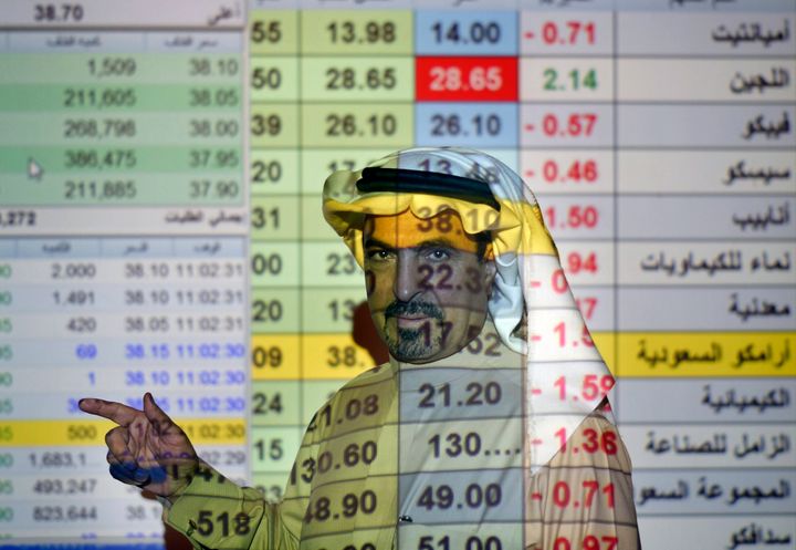 File photo of a trader talks to others in front of a screen displaying Saudi stock market values at the Arab National Bank in Riyadh, Saudi Arabia. 