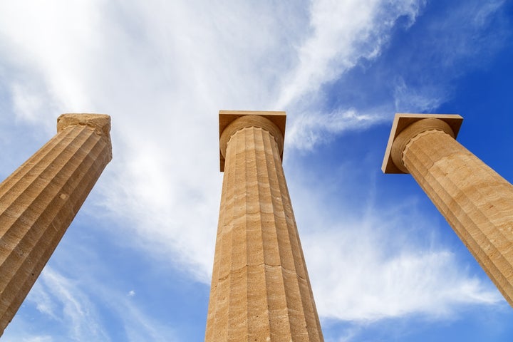 Three ancient greek pillars against a blue sky