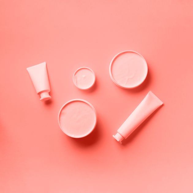 Cosmetics, skin care, beauty, body treatment concept. White cosmetic jar, tube, bottle and tropical monstera leaf over trendy coral color background. Top view. Flat lay. Mock-up