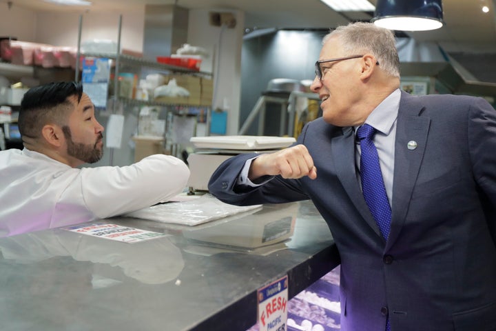 Washington Gov. Jay Inslee, right, bumps elbows with a worker at a seafood counter in Seattle on March 3. Inslee said he's doing the elbow bump with people instead of shaking hands to prevent the spread of germs, and that his visit to the store was to encourage people to keep patronizing businesses during the outbreak.