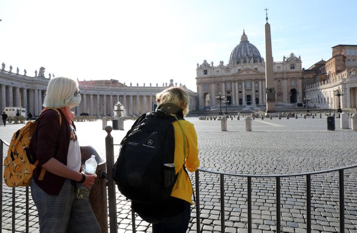 People stand behind barriers on Tuesday after the Vatican's Saint Peter's Square and its main basilica were closed to tourists as part of control measures against the spread of COVID-19.