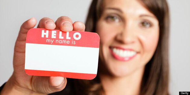 A pretty young woman holding a 'Hello My Name Is' name tag against a white background.