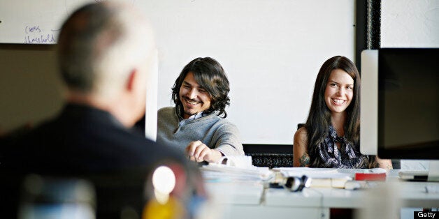 Coworkers sitting at workstation in high tech startup office in discussion with mature businessman laughing