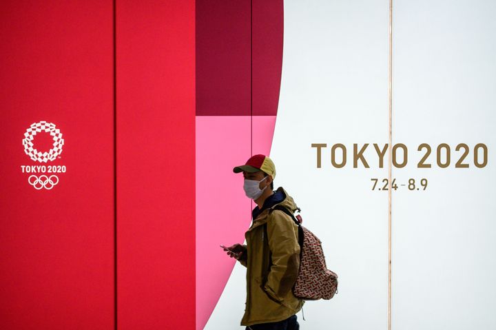 A man wearing a face mask walks in the tunnel of a metro station with the board of the official 2020 Summer Olympics advertisment in Tokyo on March 11, 2020. 