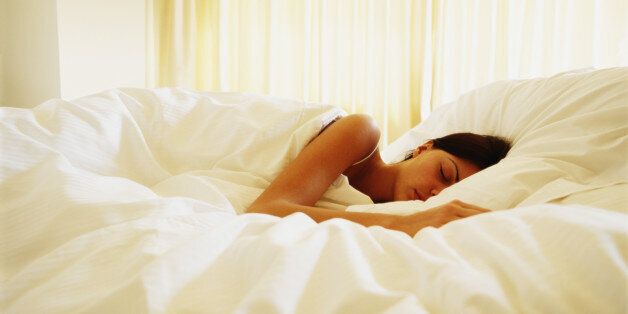 Woman lying under covers in bed, eyes closed