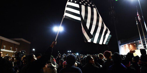A protester waves a 'black and white' modified US flag during a march following the grand jury decision in the death of 18-year-old Michael Brown in Ferguson, Missouri, on November 24, 2014. Protesters set buildings ablaze and looted stores in the US town of Ferguson on November 24 after a grand jury chose not to press charges against a white officer who shot dead a black teen. US President Barack Obama and the family of late 18-year-old Michael Brown appealed in vain for calm after a prosecutor said a grand jury had found the policeman acted in self-defense. AFP PHOTO/Jewel Samad (Photo credit should read JEWEL SAMAD/AFP/Getty Images)