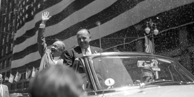 Gen. Dwight D. Eisenhower waves to confetti-tossing crowds lining the parade route to Detroit's City Hall, June 14, 1952, where he made a non-political Flag Day address. A mammoth flag, said to be the largest American flag in the world, covers the front of a large department store in the background. Man in the front of the car is unidentified. (AP Photo)