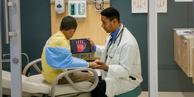 Surgeon with child in exam room explaining PET Scans (Positron emission tomography) using a tablet.
