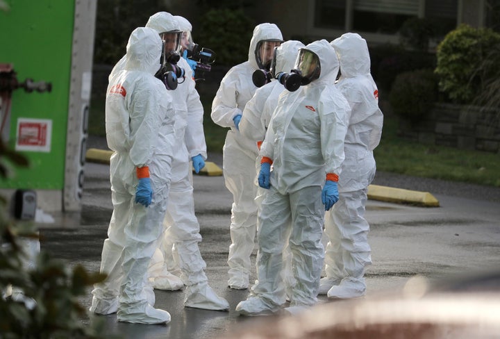 Workers wearing protective suits and respirators wait outside the Life Care Center in Kirkland, Wash., to begin cleaning and 