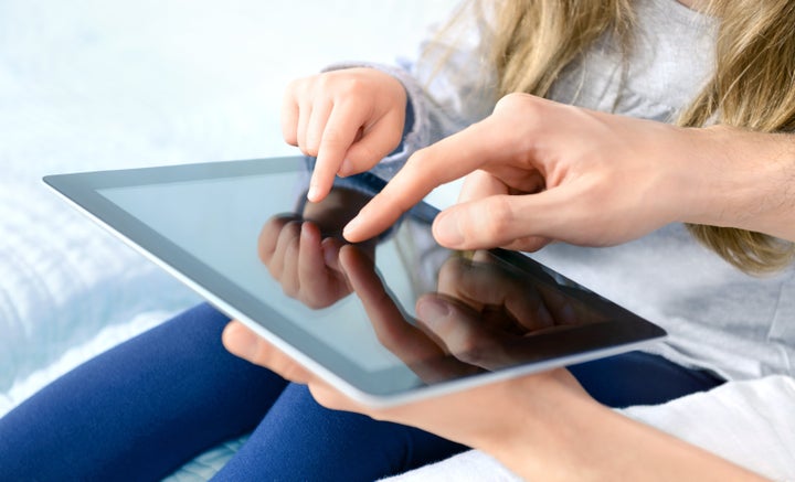 Father with daughter playing on digital tablet. Selective focus on the child's finger.