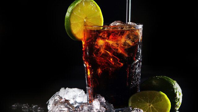 Fresh cola drink with ice and green lime on black background