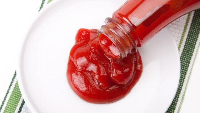 Bright red ketchup is being poured from the bottle. From above. Selective focus.