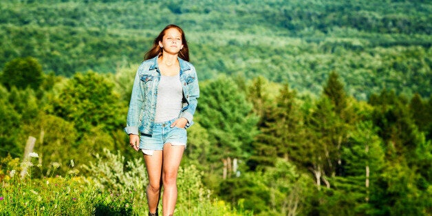 A teenager walks alone on a dirt road, lit by a Summer sunset. She smiles as she breathes in the fresh air.