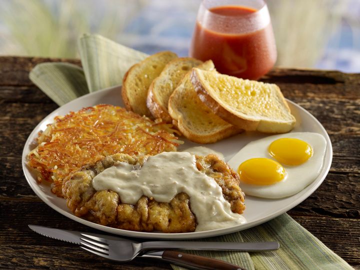 Chicken fried steak smothered in gravy with two eggs, hash browns, toast and a glass of tomato juice in an outdoor summer beach setting