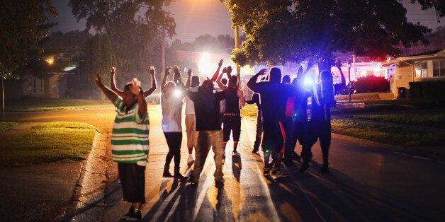 FERGUSON, MO - AUGUST 11: With their hands raised, residents gather at a police line as the neighborhood is locked down following skirmishes on August 11, 2014 in Ferguson, Missouri. Police responded with tear gas as residents and their supporters protested the shooting by police of an unarmed black teenager named Michael Brown who was killed Saturday in this suburban St. Louis community. Yesterday 32 arrests were made after protests turned into rioting and looting in Ferguson. (Photo by Scott Olson/Getty Images)