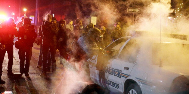 A police officer approach a police vehicle after a protester has thrown a smoke device from the crowd Tuesday, Nov. 25, 2014, in Ferguson, Mo. Missouri's governor ordered hundreds more state militia into Ferguson on Tuesday, after a night of protests and rioting over a grand jury's decision not to indict police officer Darren Wilson in the fatal shooting of Michael Brown, a case that has inflamed racial tensions in the U.S. (AP Photo/David Goldman)