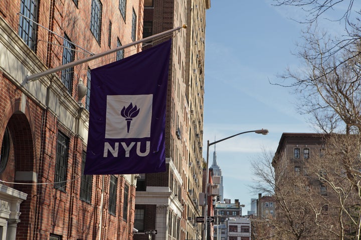 New York, MY, USA - March 22, 2016: New York University buildings on Macdougal Street at 37 Washington Square West. A purple flag with the NYU logo hangs above an entrance to one of the college buildings. In the distance, the Empire State Building appears above buildings on West 8th Street.