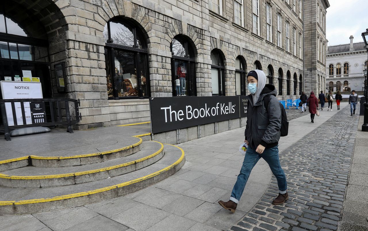 A man in a protective mask walks past the entrance to the Book of Kells building, usually crowded with tourists, following the announcement that Trinity College will close many tourist attractions within the college in Dublin.