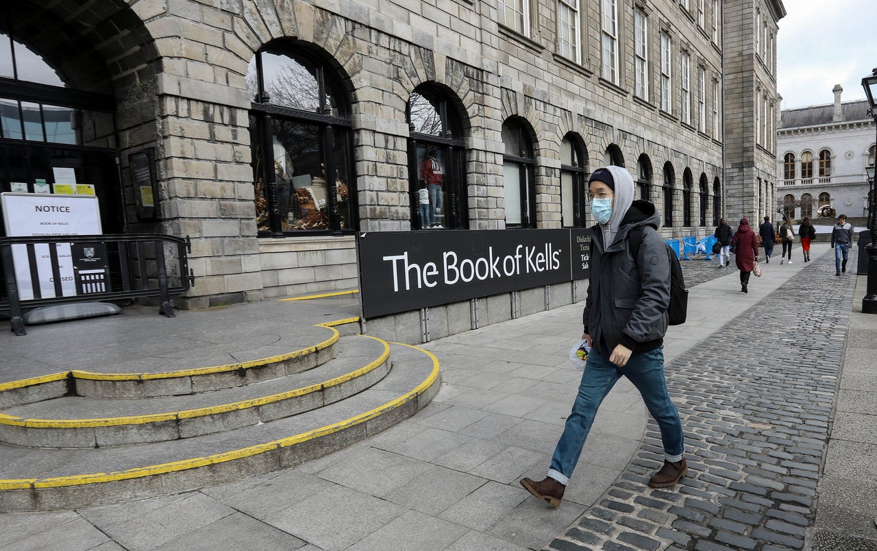 A man in a protective mask walks past the entrance to the Book of Kells building, usually crowded with tourists, following the announcement that Trinity College will close many tourist attractions within the college in Dublin.