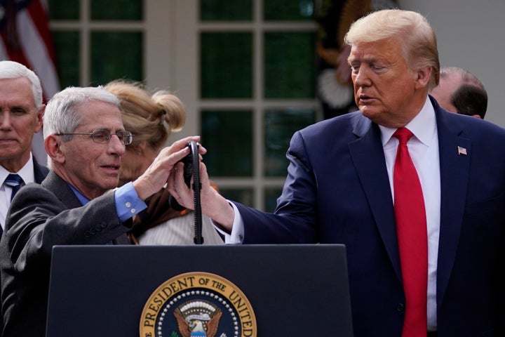 President Donald Trump adjusts the microphone for Dr. Anthony Fauci, director of the National Institute of Allergy and Infect