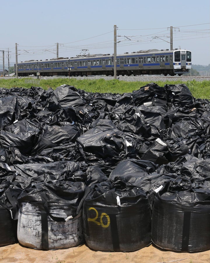 避難区域で初の鉄道運行を再開したJR常磐線・広野―竜田駅間を走行する列車。手前は集められた除染で出た汚染土など＝6月1日午前、福島県楢葉町