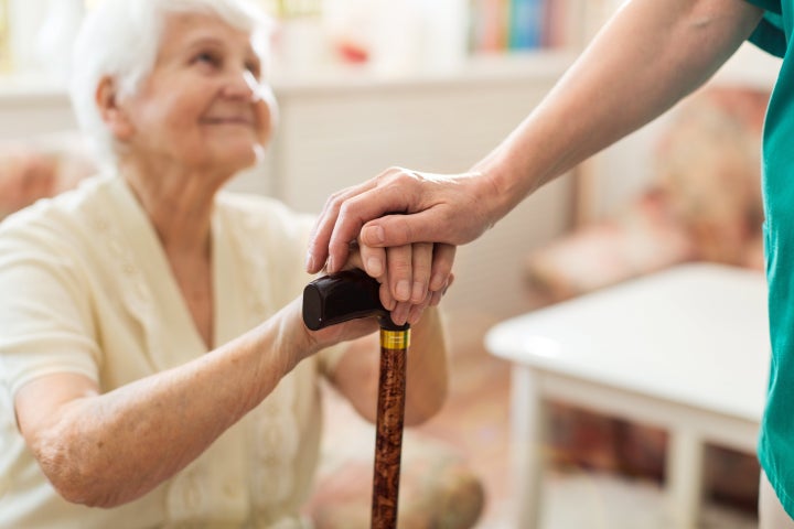 Close-up of woman holding senior's hands leaning on cane