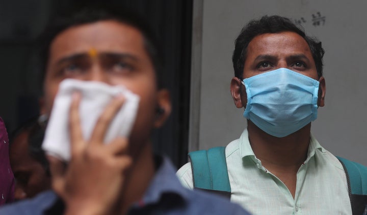 Indians cover their faces as they watch the stock exchange index at the BSE building in Mumbai on March 12, 2020. Global shares plunged Thursday after the WHO declared a coronavirus pandemic and indexes sank on Wall Street. 