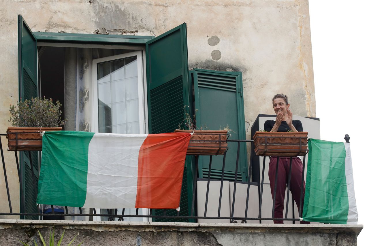 A woman applauds as she stands on her balcony adorned with the Italian flag, at the Garbatella neighborhood, in Rome, Saturday, March 14, 2020.