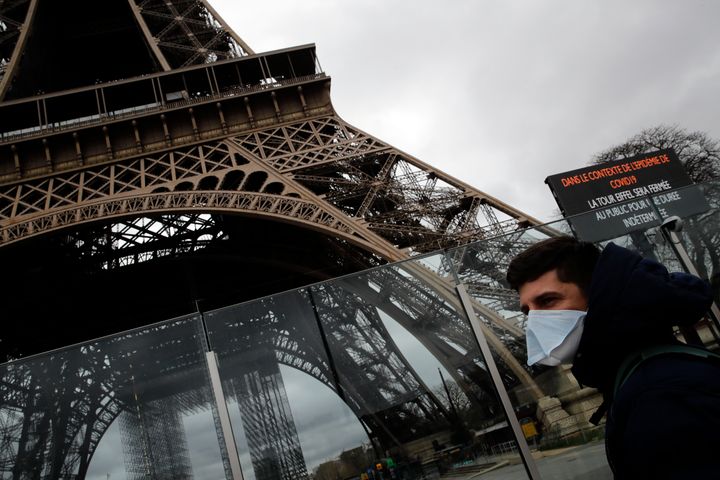 A man wearing a mask walks pasts the Eiffel tower closed after the French government banned all gatherings of over 100 people to limit the spread of the virus COVID-19, in Paris, Saturday, March 14, 2020.