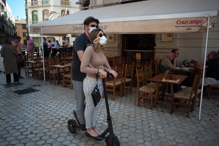 A couple wearing face masks as a precaution against the spread of coronavirus ride a scooter in downtown Malaga.