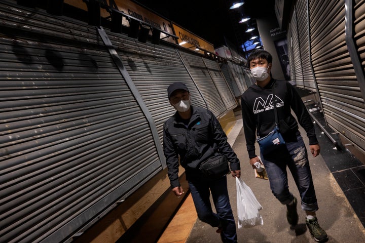 Tourists wearing masks walk past closed stalls at La Boqueria market in Barcelona, Spain, Saturday, March 14, 2020.