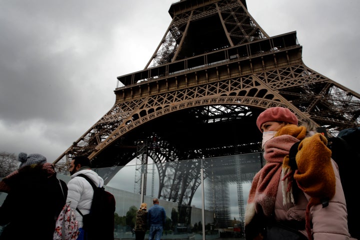 A woman wearing a mask walks pasts the Eiffel Tower closed after the French government banned all gatherings of over 100 people to limit the spread of the virus COVID-19, in Paris, Saturday, March 14, 2020. (AP Photo/Christophe Ena)