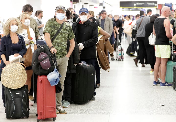 Travelers wearing surgical masks wait in line, Friday, March 13, 2020, at Miami International Airport in Miami. (AP Photo/Wilfredo Lee)