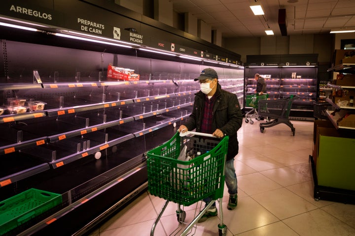 A man wearing a mask walks past empty shelves in a meat market in Barcelona, Spain, Saturday, March 14, 2020. (AP Photo/Emilio Morenatti)