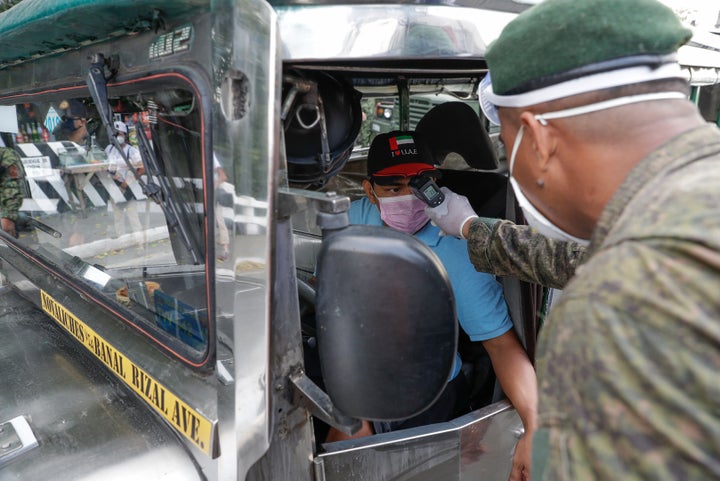 An army trooper uses a thermal scanner to check the temperature of man before entering the metropolis at a checkpoint on the outskirts of Quezon city, Philippines Sunday, March 15, 2020. (AP Photo/Aaron Favila)