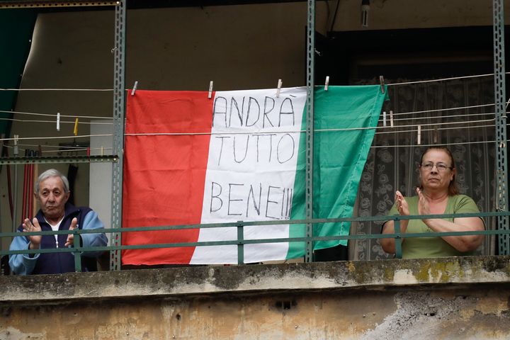 A couple applauds next to an Italian flag reading everything will be alright, at the Garbatella neighborhood, in Rome, Saturday, March 14, 2020. (AP Photo/Alessandra Tarantino)