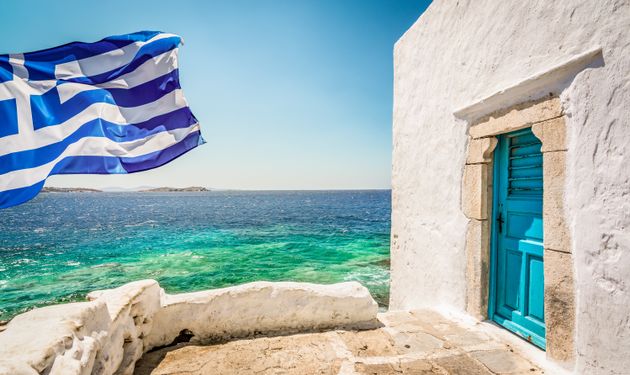 Bright and colorful image of Greek National Flag on Mykonos Island. White building with blue door at...
