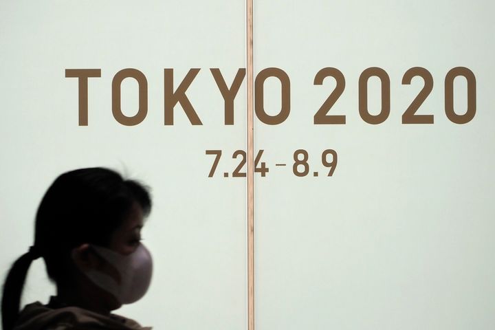 A woman walks past a large display promoting the Tokyo 2020 Olympics in Tokyo, Friday, March 13, 2020.