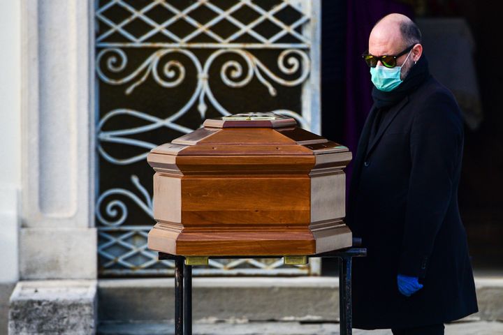 A man wearing a face mask stands by the coffin of his mother during a funeral service in the closed cemetery of Seriate, near Bergamo, Lombardy, on March 20, 2020 during the country's lockdown aimed at stopping the spread of the COVID-19 (new coronavirus) pandemic. (Photo by Piero Cruciatti / AFP) (Photo by PIERO CRUCIATTI/AFP via Getty Images)