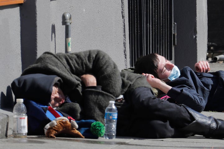 A man wearing a mask sleeps near another person on a sidewalk near the Union Gospel Mission on Friday.