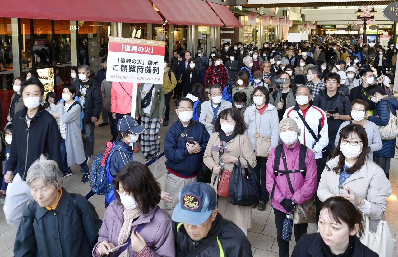 People wearing protective face masks queue as they try to watch the Olympic cauldron during the Tokyo 2020 Olympics Flame of Recovery tour in Japan.